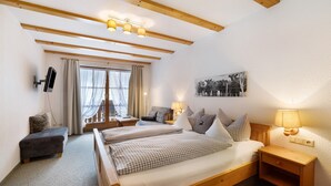 Ein Schlafzimmer mit zwei Betten, einem Schreibtisch, einem Stuhl, einem Fernseher und einem Fenster mit Vorhängen.