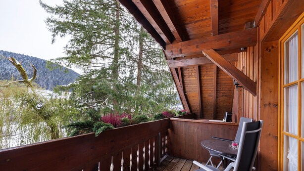 Eine Holzterrasse mit Tisch und Stühlen mit Blick auf ein bewaldetes Gebiet und einen See.