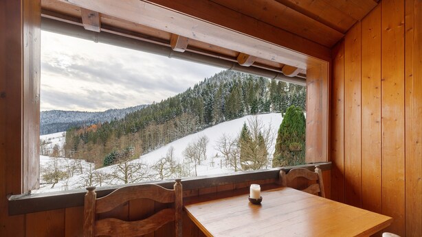 Ein Holzinnenraum mit Tisch und Stühlen, ein Fenster mit Blick auf eine verschneite Landschaft.