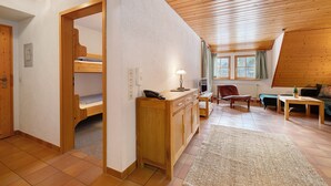Ein Zimmer mit Etagenbett, einem Holztisch, einem Stuhl und einem kleinen Tisch mit Lampe.