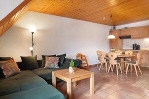 A cozy living area with a wooden ceiling, a green sofa, a wooden dining table, and a kitchen in the background. - Apartment 'Kinzigstuben' with Mountain View, Shared Terrace and Wi-Fi (Alpirsbach)