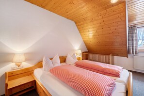 A bedroom with two beds, wooden headboard, bedside tables with lamps, and a window with curtains. - Apartment 'Kinzigstuben' with Mountain View, Shared Terrace and Wi-Fi (Alpirsbach)