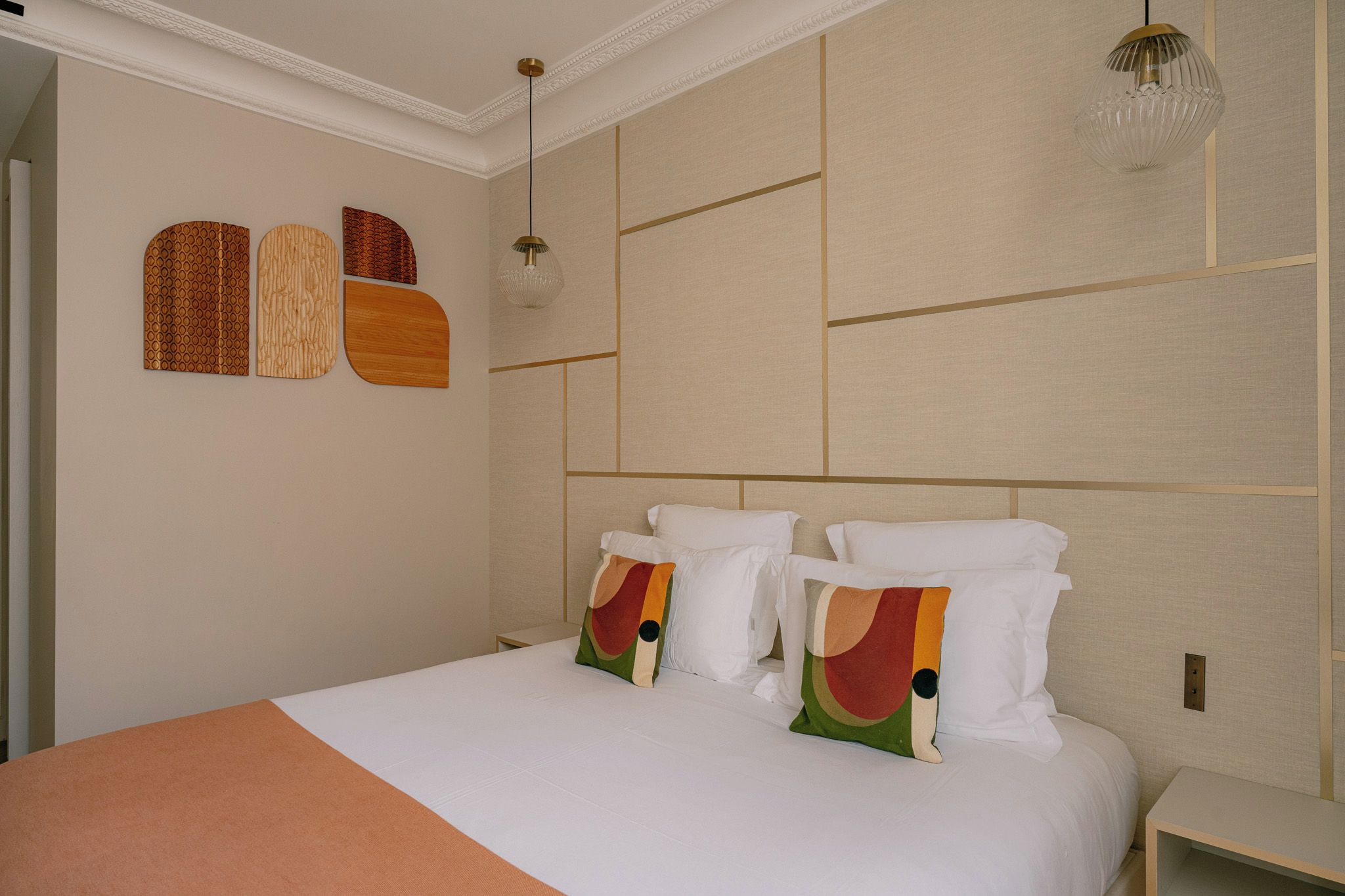 Quarto de hotel com uma cama grande, duas mesas de cabeceira, uma parede com padrões geométricos e um lustre.