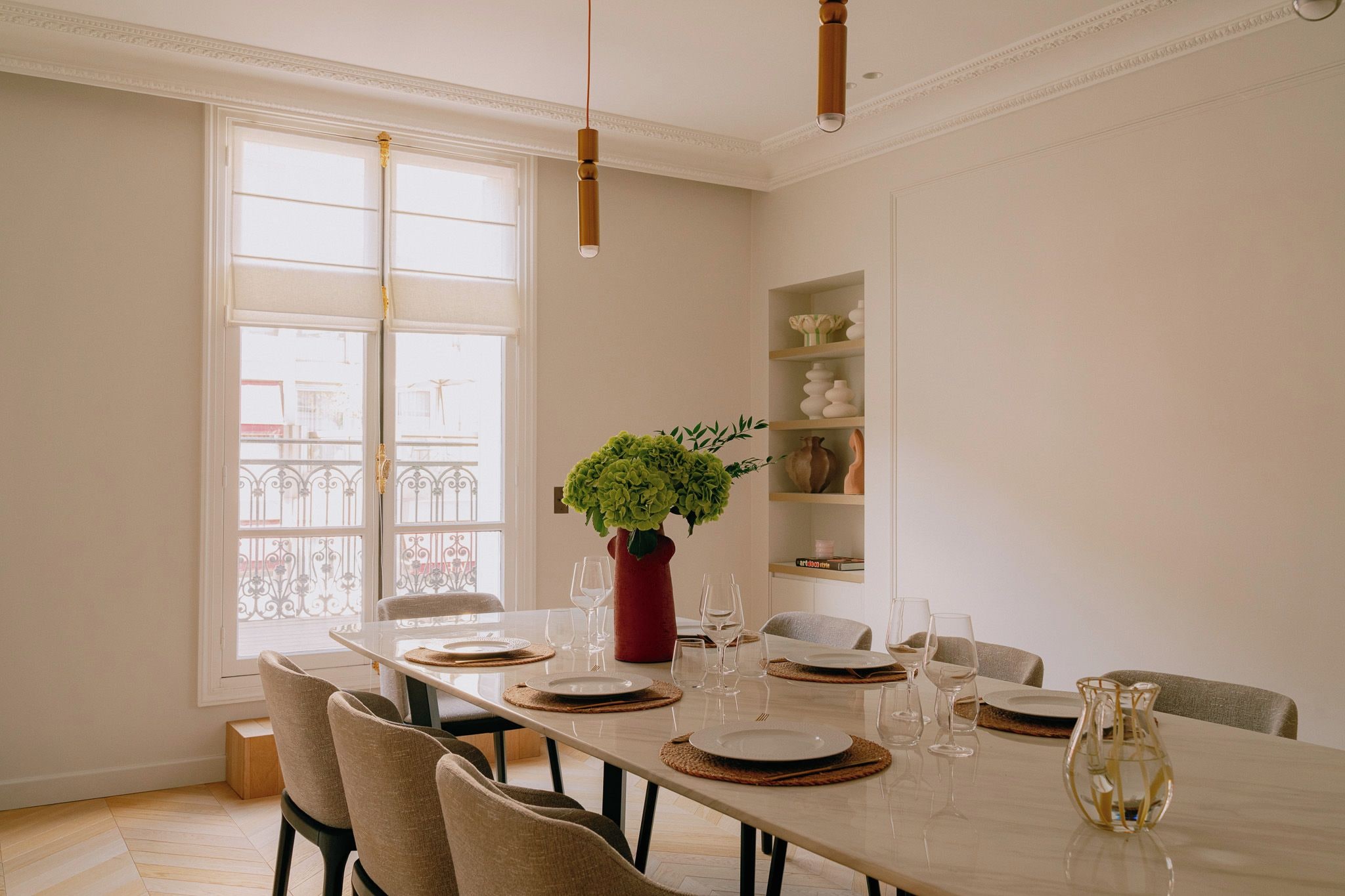 A dining area with a table set for six, a potted plant, and a shelf with decorative items.