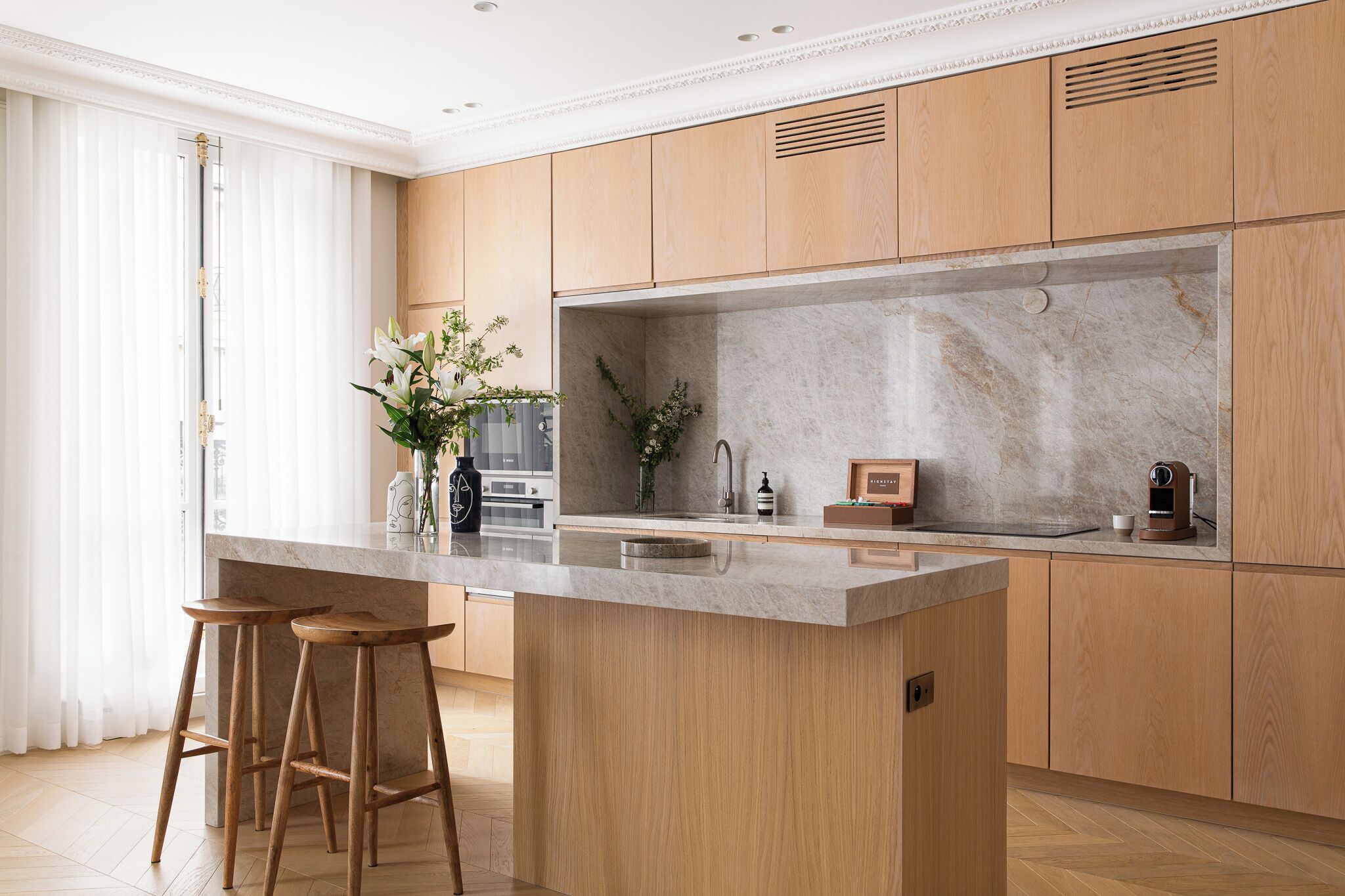 Eine moderne Küche mit Holzausstattung, einer Marmorarbeitsplatte und zwei Barhocker.