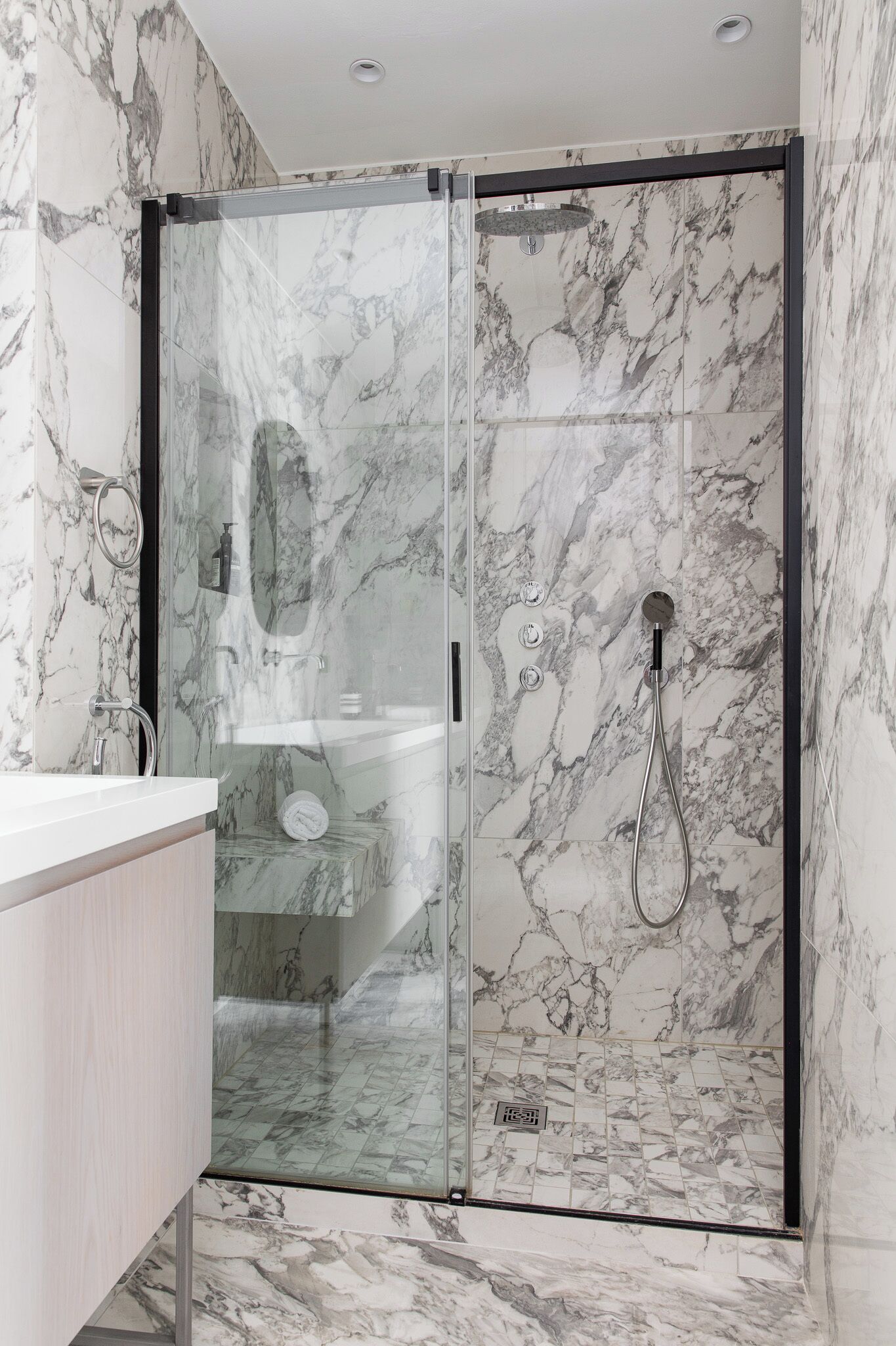 A modern bathroom with a glass-enclosed shower, marble walls, and a white sink.
