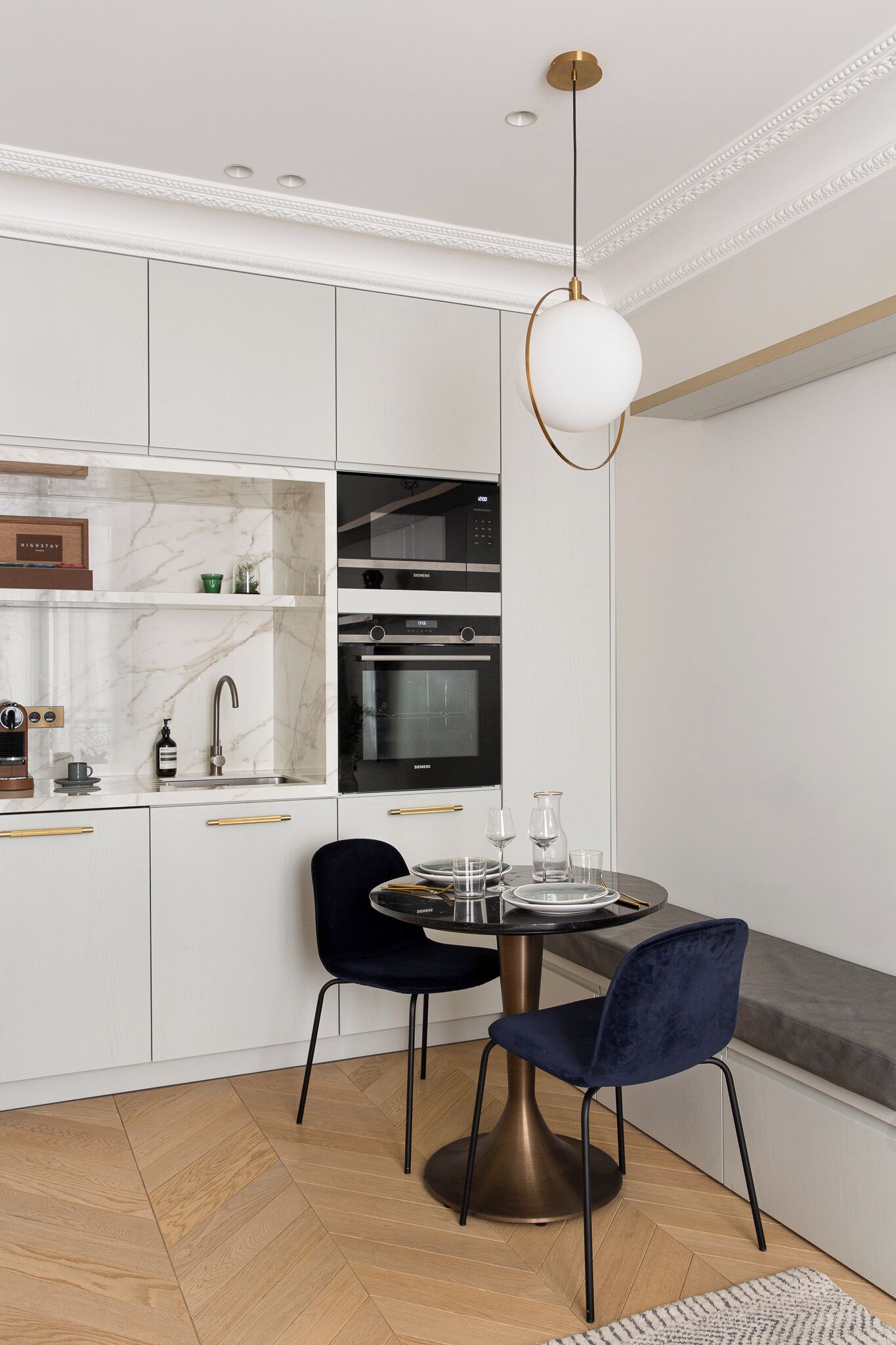 A modern kitchen with white cabinetry, a black countertop, and a round dining table with two chairs.