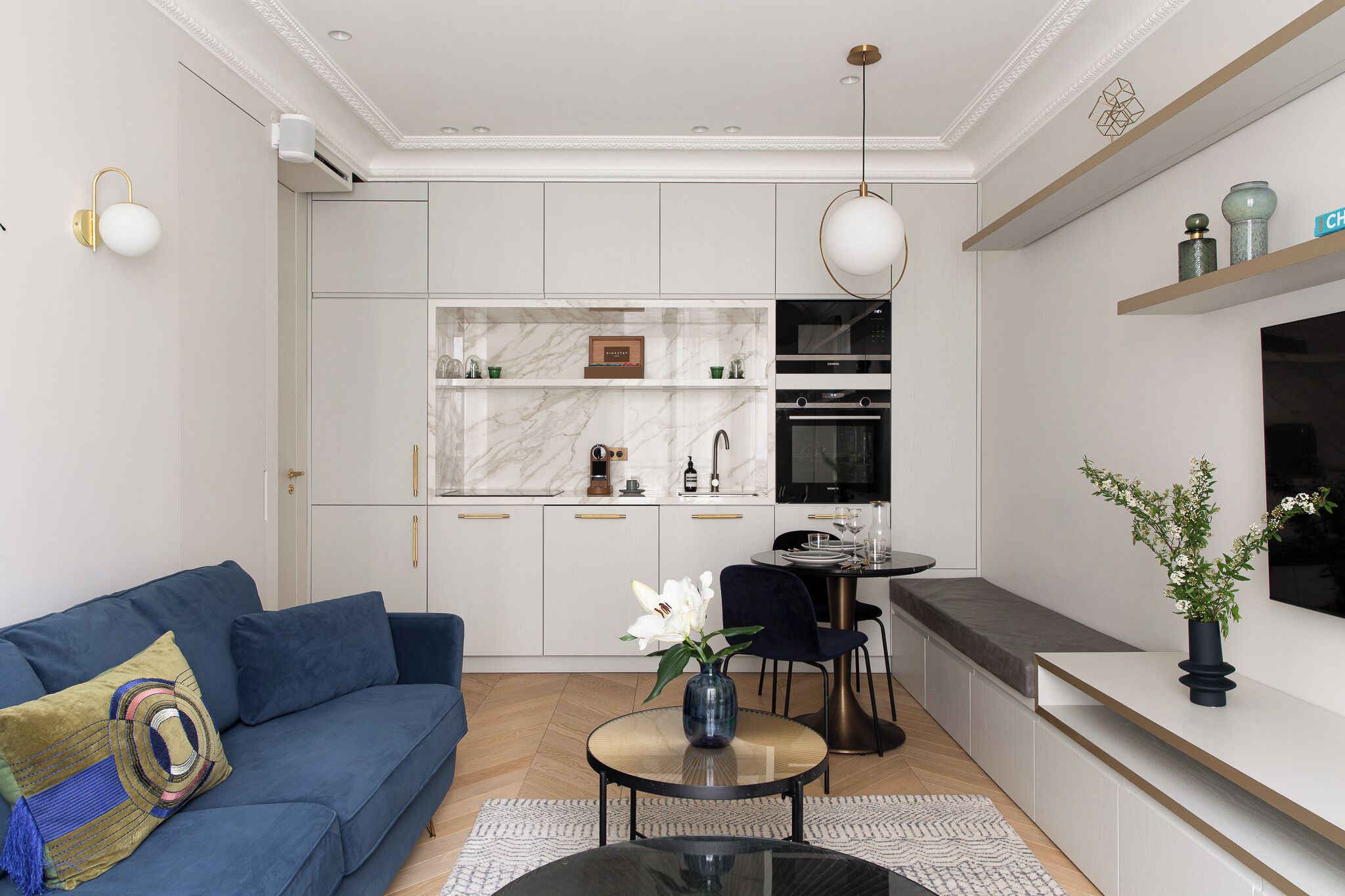A modern kitchen with white cabinets, a marble countertop, and a built-in oven.