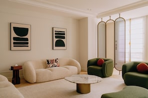Ein modernes Wohnzimmer mit einem beigen Sofa, einem grünen Sessel, einem runden Couchtisch und abstrakter Kunst an der Wand.