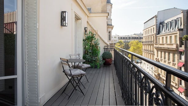 A balcony with a table and chairs, a potted plant, and a view of surrounding buildings. - HIGHSTAY - Appartements de luxe - Arc de Triomphe (Paris)