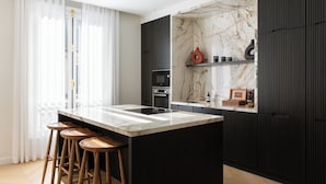 A modern kitchen with a marble countertop, black cabinetry, and wooden stools. - HIGHSTAY - Appartements de luxe - Arc de Triomphe (Paris)