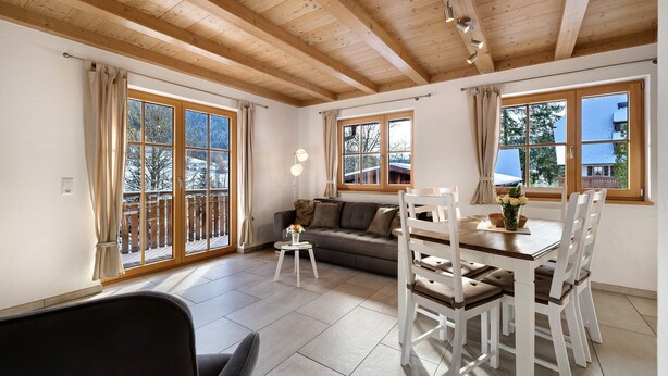 Una habitación con techo de madera, ventanas amplias, un sofá, una mesa de comedor con sillas y una pequeña mesita con un jarrón.