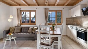 Cocina moderna con armarios de madera, una mesa de comedor y un sofá en un espacio luminoso con ventanas amplias.