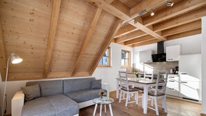 Un espacio tipo loft con techo de madera, un sofá modular gris, una mesa de comedor con sillas y una zona de cocina.