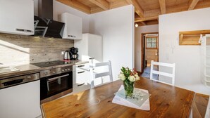 Una cocina moderna con vigas de madera, muebles blancos, una estufa de acero inoxidable y un comedor con mesa y sillas de madera.