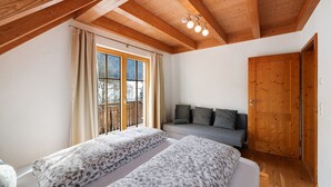 Un dormitorio con dos camas, un sofá, techo de madera y un ventanal grande.