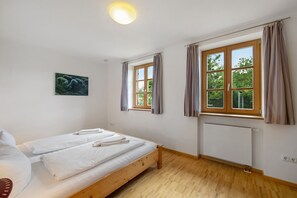 Una habitación con cama, ventana, radiador y un cuadro en la pared.