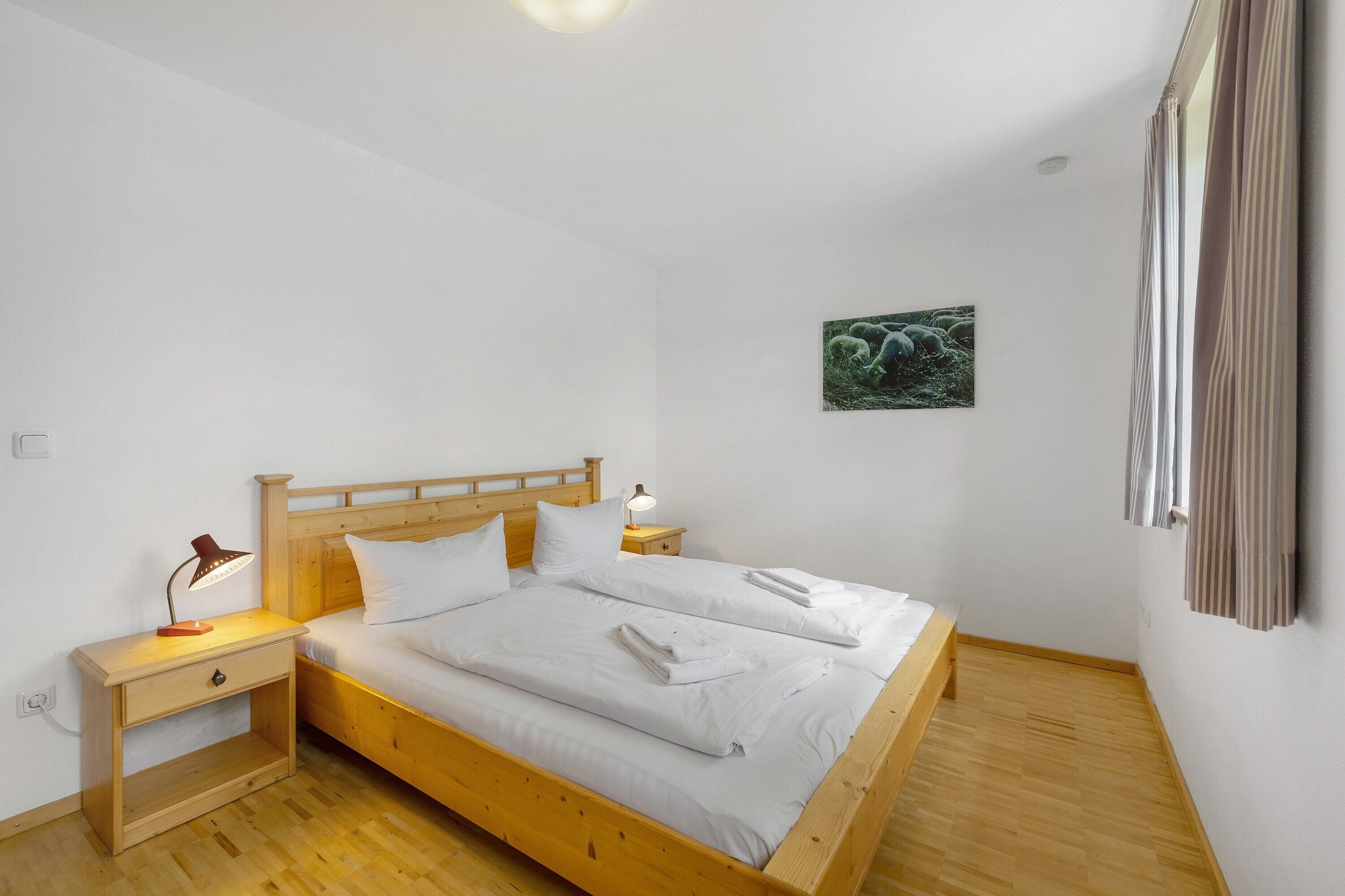 Un letto singolo con struttura in legno, biancheria bianca, un comodino con una lampada e una piccola mensola.