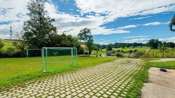 A soccer field with a goalpost, a paved walkway, and a grassy area with trees and a clear sky.