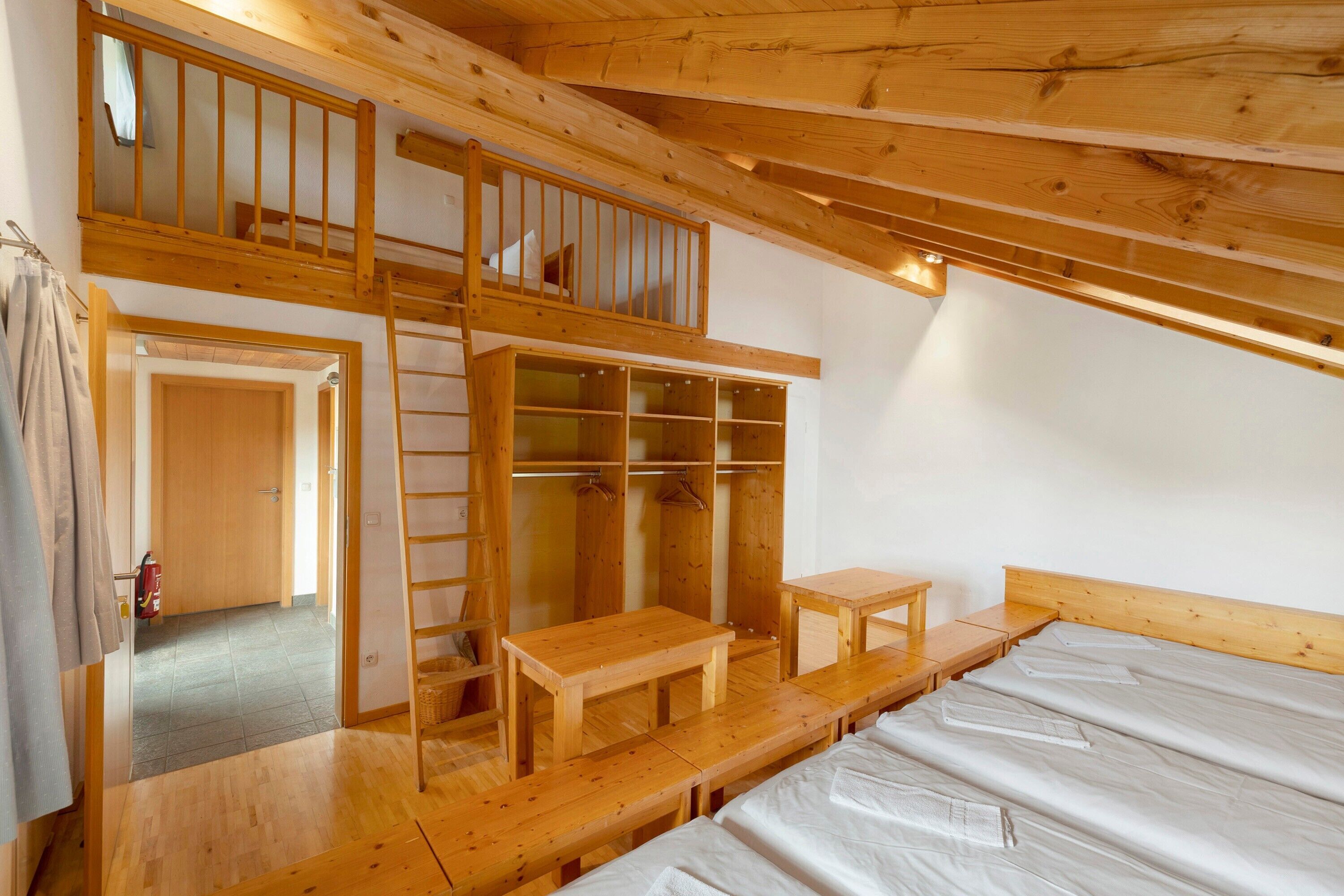 Een houten interieur met een slaapkamer op een entresol, een houten bank en een houten tafel.