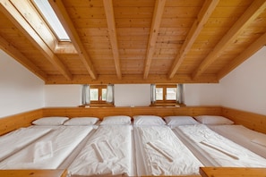 Quarto com teto inclinado, vigas de madeira e quatro camas dispostas em linha.