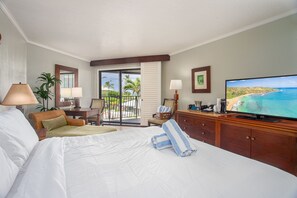 A hotel room with a bed, a TV, a desk with a lamp, a chair, and a view of the ocean. - Watch Pacific Ocean sunrise from the comfort of your private ocean view lanai! (Lihue)