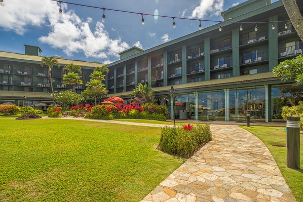 A multi-story hotel with a central courtyard, outdoor seating, and a stone pathway. - Watch Pacific Ocean sunrise from the comfort of your private ocean view lanai! (Lihue)