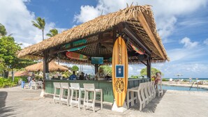 Een tiki bar met rieten dak, barstoelen en uitzicht op het zwembad.