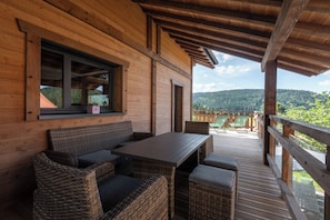 A wooden deck with wicker furniture, a table, and chairs, overlooking a mountainous landscape. - ✨ Chalet L'Anahi ⭐⭐⭐⭐⭐ – 5-Star Luxury Chalet with Panoramic Mountain Views (Gérardmer)