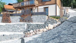 Uma casa moderna de madeira com dois andares, varanda, muro de pedra e entrada com piso pavimentado.