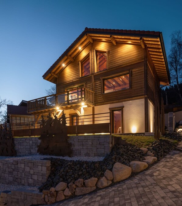 A two-story wooden house with a balcony and a stone wall in front.