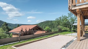 Um deck de madeira com vista para um edifício de telhado vermelho e uma colina arborizada.
