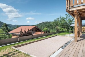 Una terraza de madera con vistas a un edificio de techo rojo y una colina arbolada.