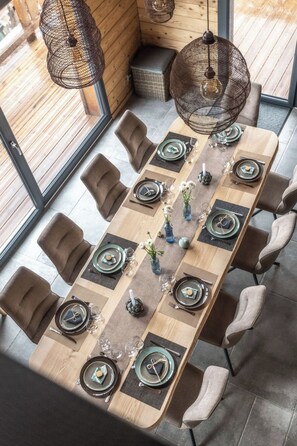 Un comedor con una mesa larga dispuesta para seis personas, rodeada de sillas, con lámparas colgantes arriba.