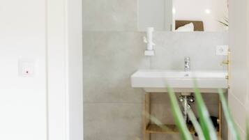 A modern bathroom with a white sink, a mirror, and a shower area.