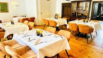 A dining area with tables set for four, each with a vase of yellow flowers, in a room with wooden flooring and white walls.