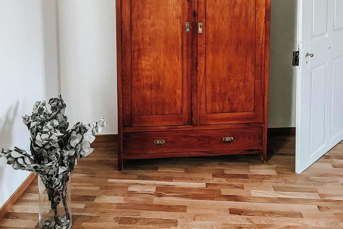 Un armario de madera con dos puertas y dos cajones, ubicado en una habitación con suelo de madera y paredes blancas.