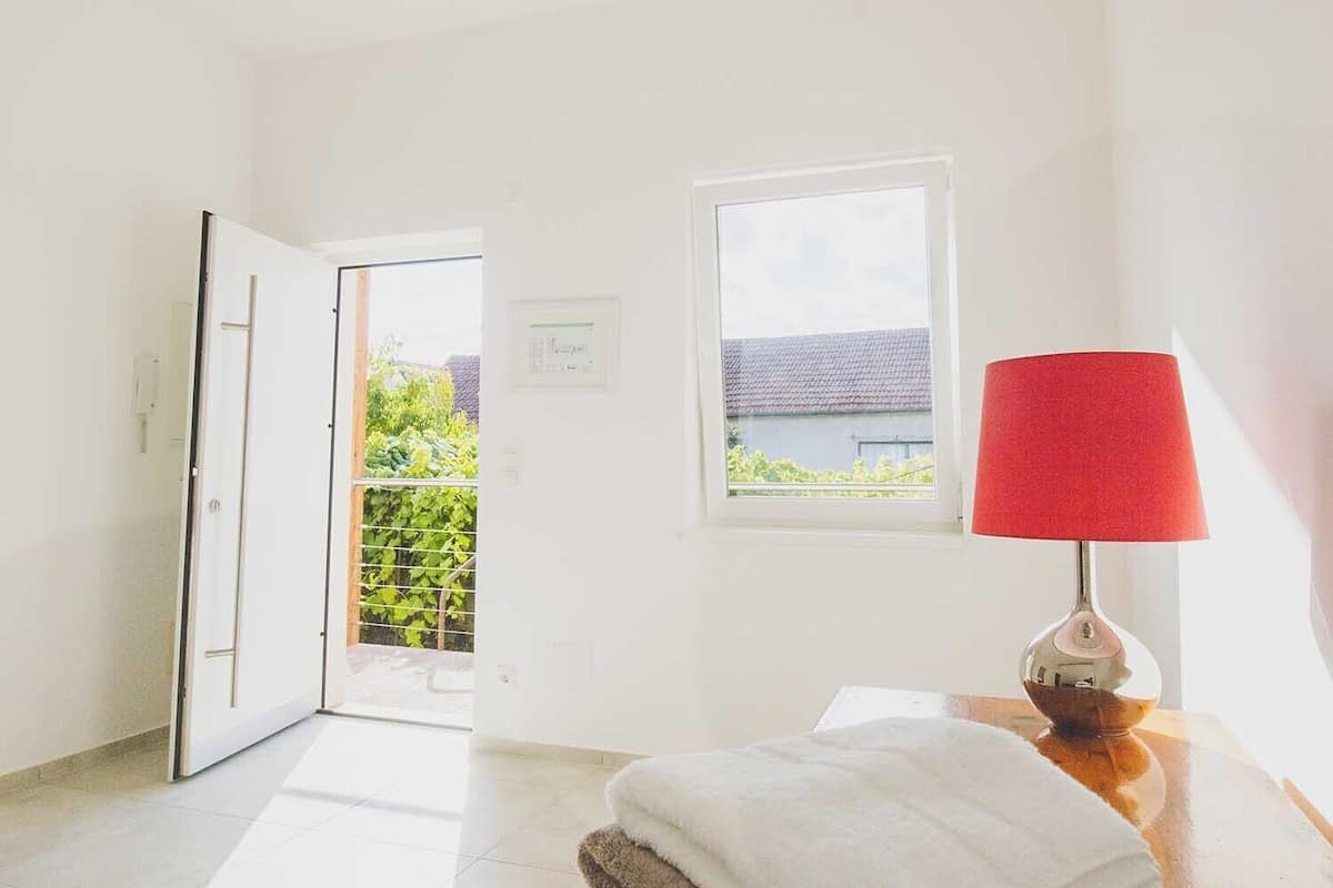 Una habitación luminosa con piso de madera, una pila de toallas, una lámpara roja y una ventana con vista a la vegetación.