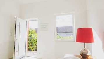 A bright room with a wooden floor, a stack of towels, a red lamp, and a window with a view of greenery.