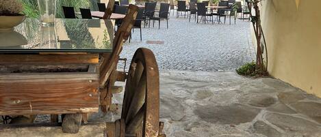 An outdoor café with stone flooring, wooden tables, and chairs.