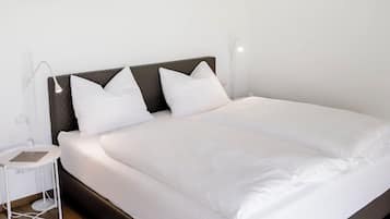 Una cama bien tendida con ropa blanca, un cabecero de madera y una mesita de noche con una lámpara.