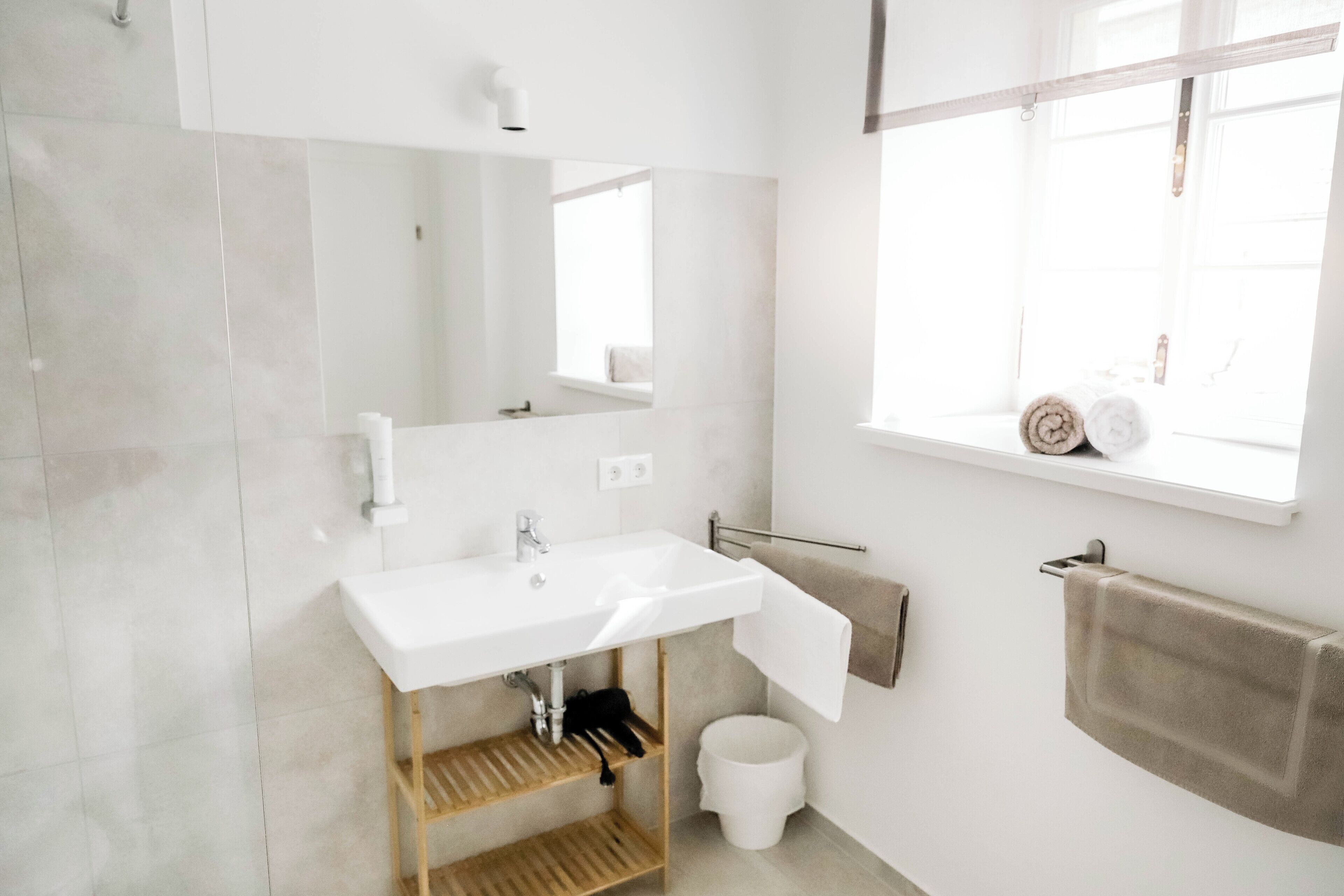 Un baño moderno con lavamanos, espejo y ventana blancos.