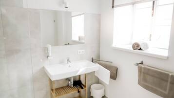 A modern bathroom with a white sink, mirror, and window.