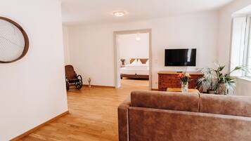 Een moderne woonkamer met een bruine bank, houten vloeren, een flatscreen televisie en een groot raam.