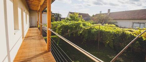 A wooden balcony with a metal railing overlooking a garden with green vines.