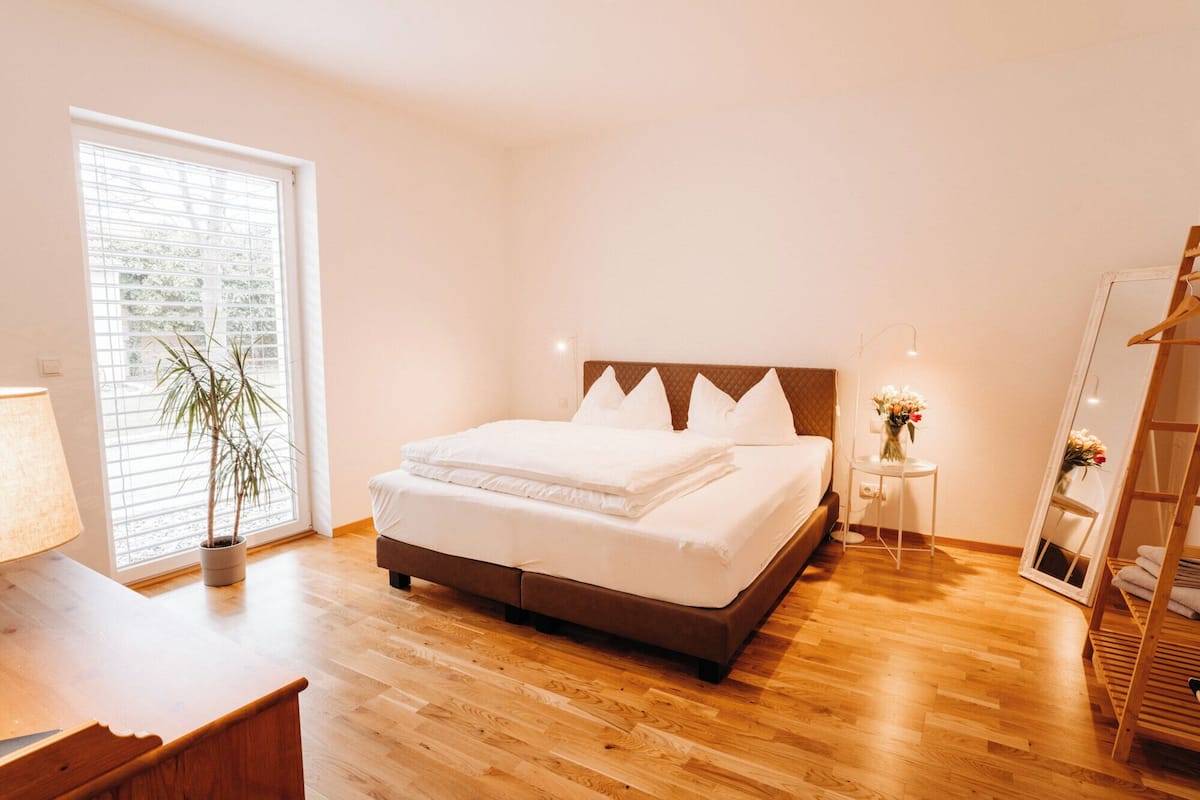 Un dormitorio ordenado con cama, mesita de noche, lámpara y una planta en maceta.