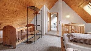 A high-ceilinged room with wooden beams, a crib, a bed, and a built-in shelf. - Apartment '8 - Flößerstuben' with Mountain View, Shared Terrace and Wi-Fi (Alpirsbach)