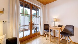 A room with a wooden floor, a table with chairs, a lamp, and a window with curtains. - Room '13' with Mountain View, Shared Terrace and Wi-Fi (Alpirsbach)