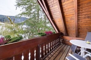 Une terrasse en bois avec une table et des chaises, donnant sur un lac, avec des arbres et des montagnes en arrière-plan.