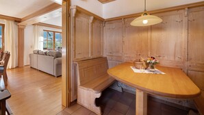 Una mesa de comedor de madera con un banco, una lámpara colgante y vistas a una sala de estar con un sofá y cortinas.
